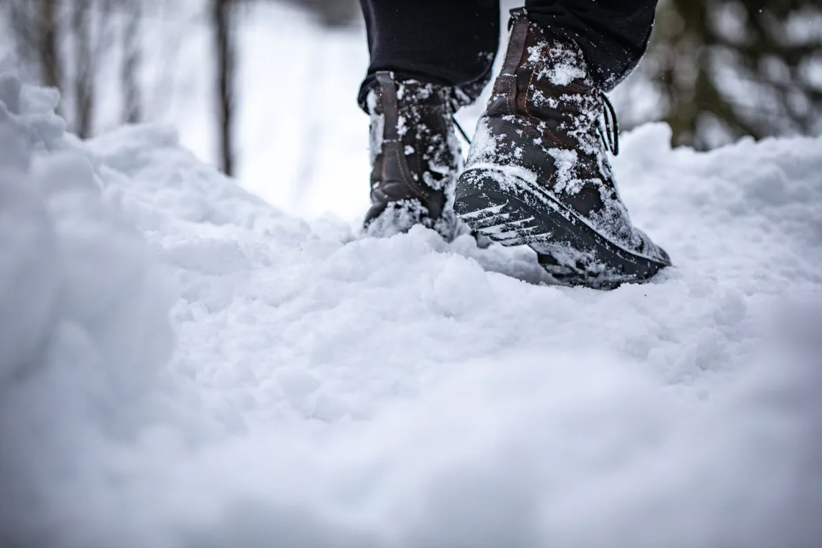 Close-up of boots stepping in deep snow, showcasing winter footwear in a snowy landscape.