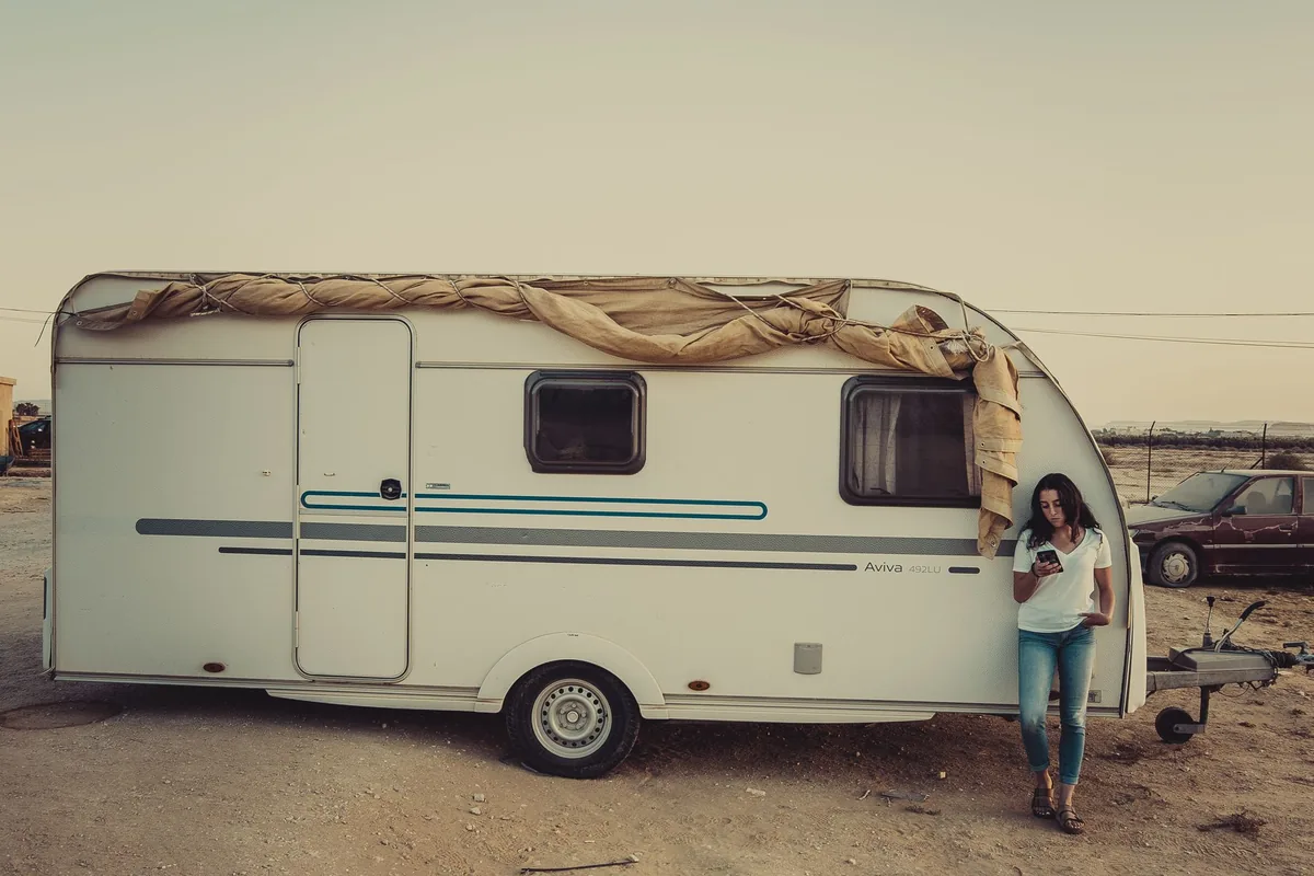 A woman stands by a camper van in a serene outdoor setting during sunset.