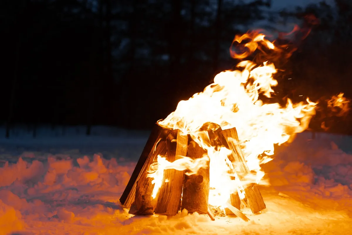 Warm campfire burning brightly in a snowy winter landscape, casting a cozy glow.