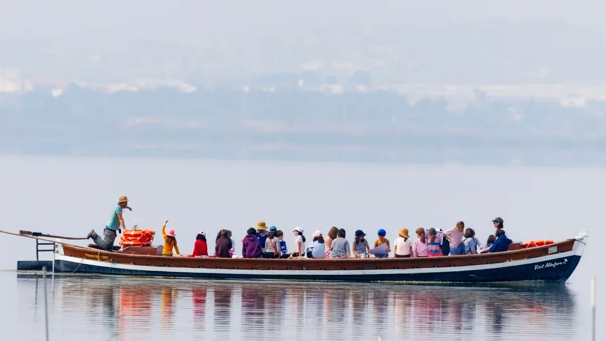 A diverse group enjoys a calm boat ride on a serene lake with scenic landscapes in the background.
