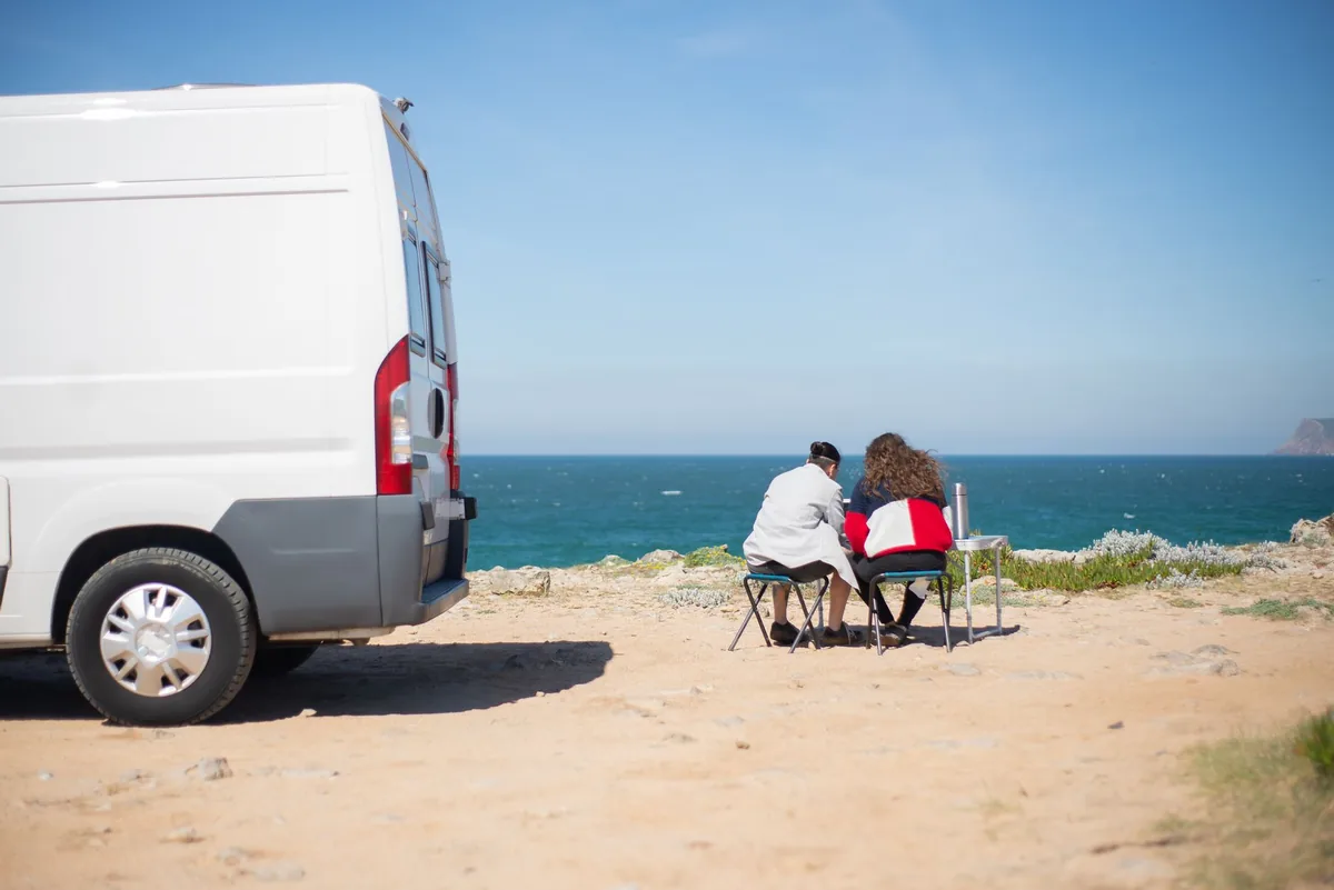 A couple enjoys a coastal view in Portugal, sitting by their camper van.