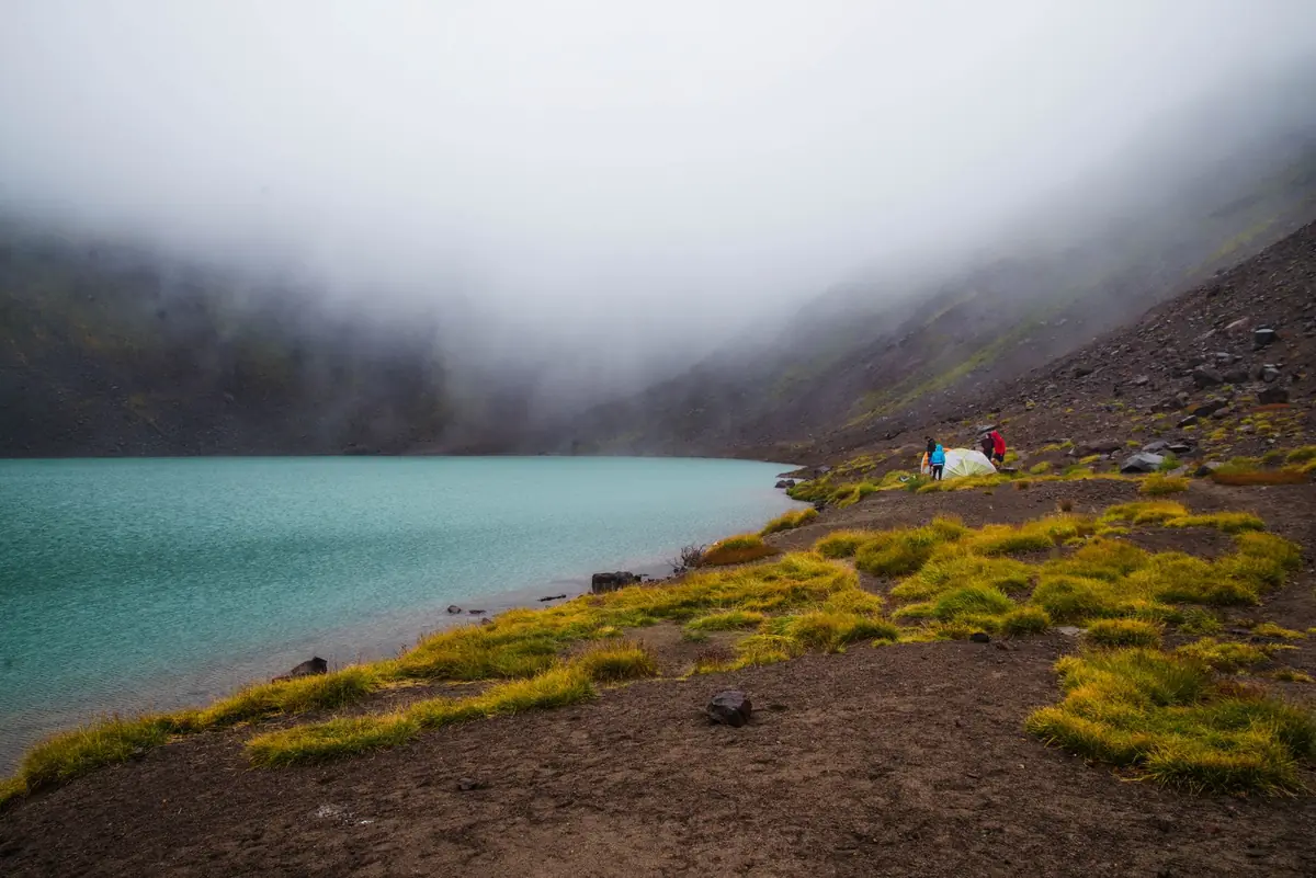 A serene foggy mountain lake with campers by the shore, showcasing nature's tranquility.