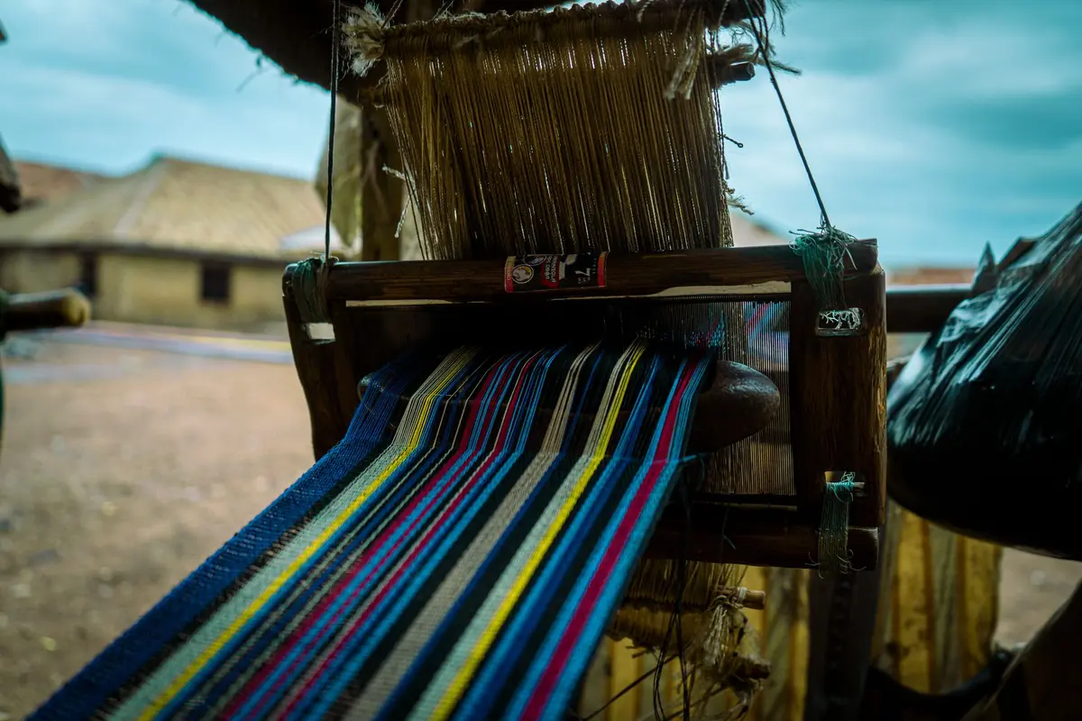 Close-up of a traditional handloom weaving a colorful textile in a rural setting.