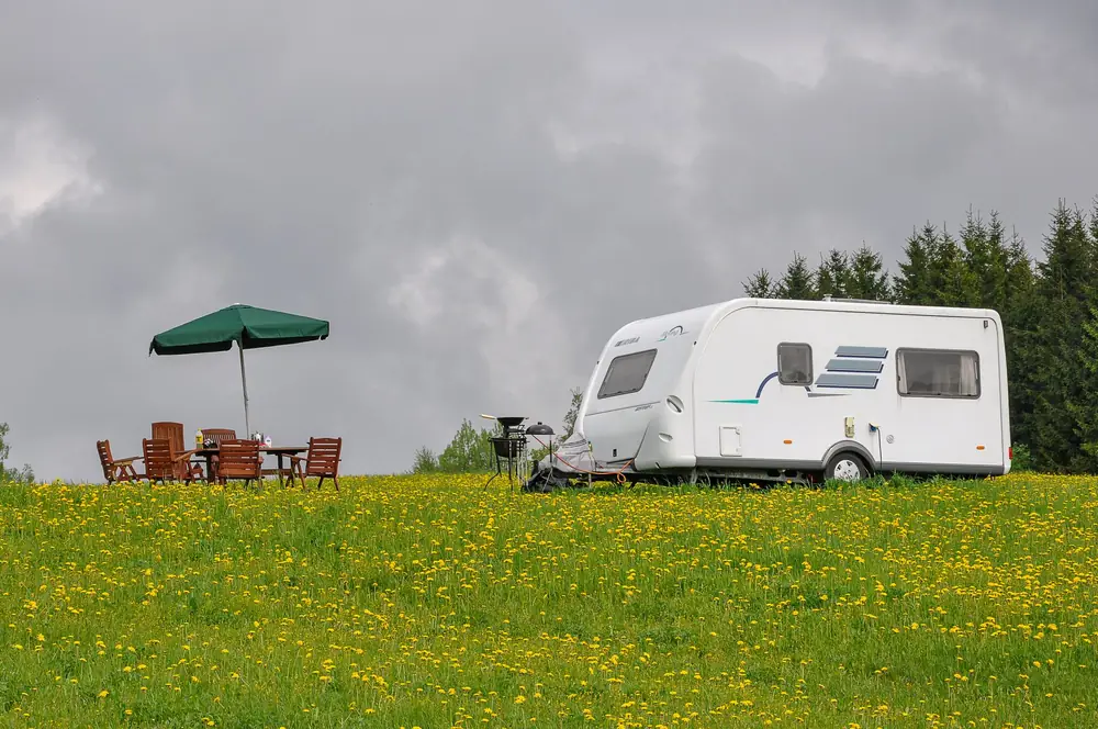Caravan in blooming dandelion field with garden setup under cloudy skies in Võru, Estonia.