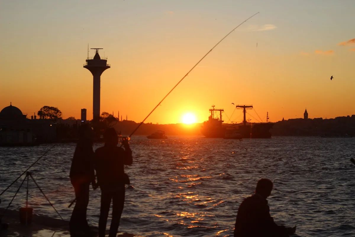 Silhouettes fishing on the Bosphorus at sunset in İstanbul, capturing a serene oceanside moment.
