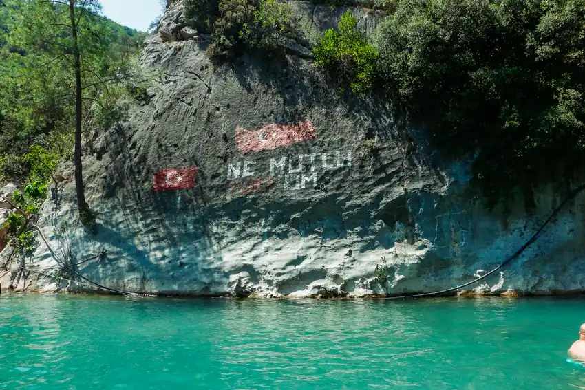 Turkish-themed mural on rock face by turquoise water in Mersin, Türkiye.