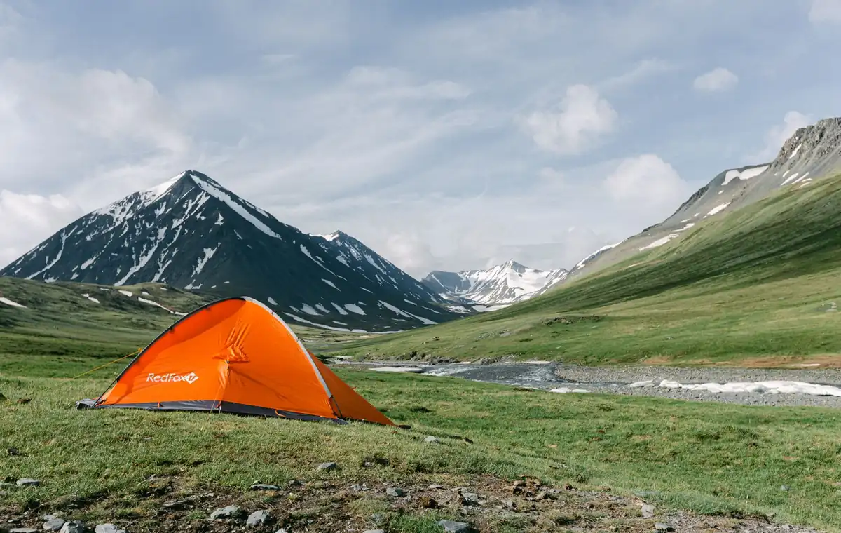 A vibrant orange tent set against a majestic mountain landscape, perfect for summer camping.
