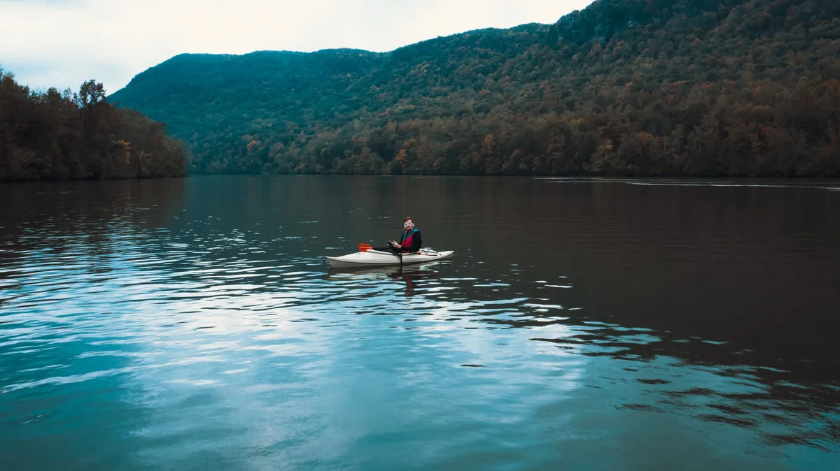 Kayaker glides on peaceful lake surrounded by mountain landscape in daytime.
