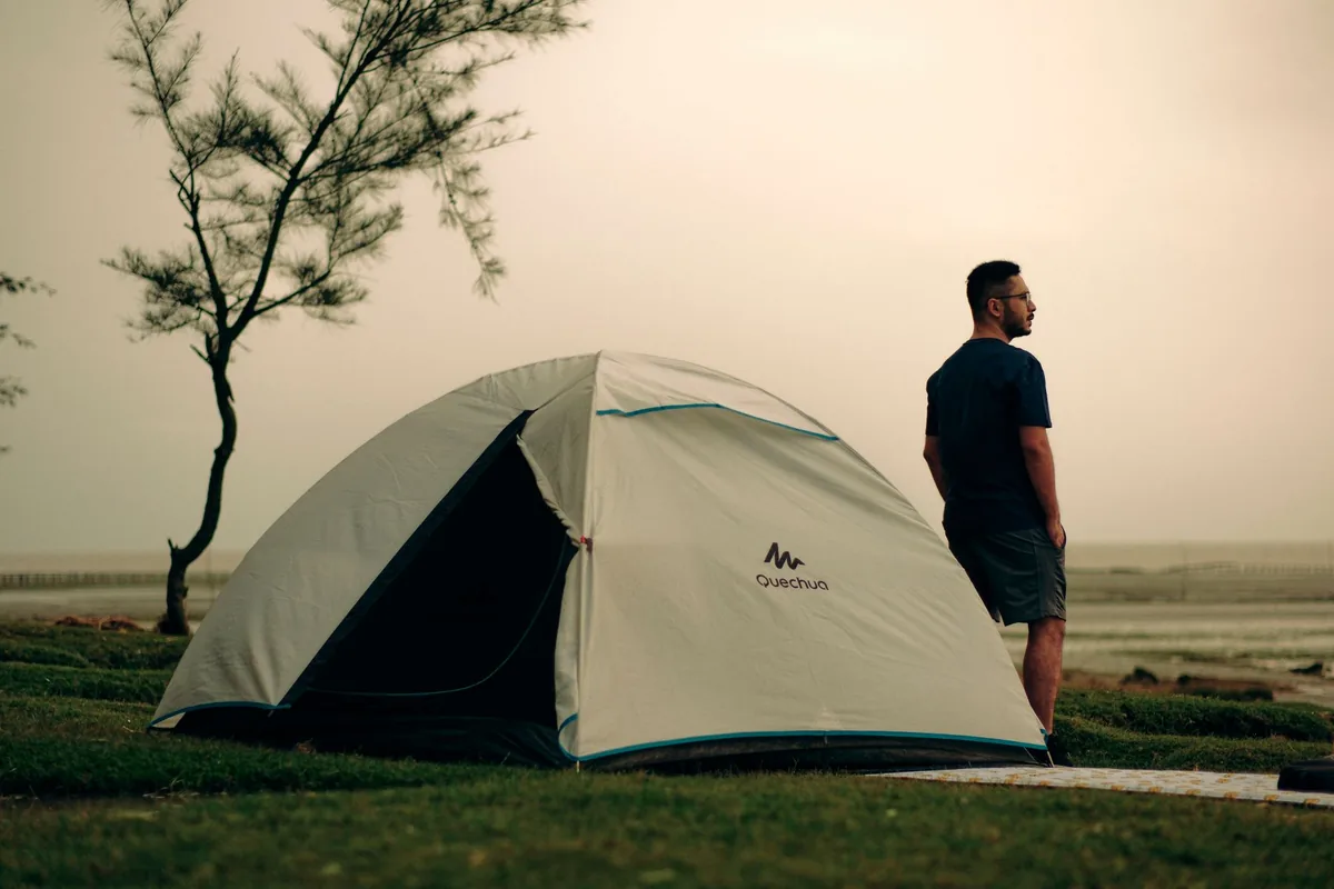 A man standing by a tent on a coastal campsite, capturing a serene sunset moment.