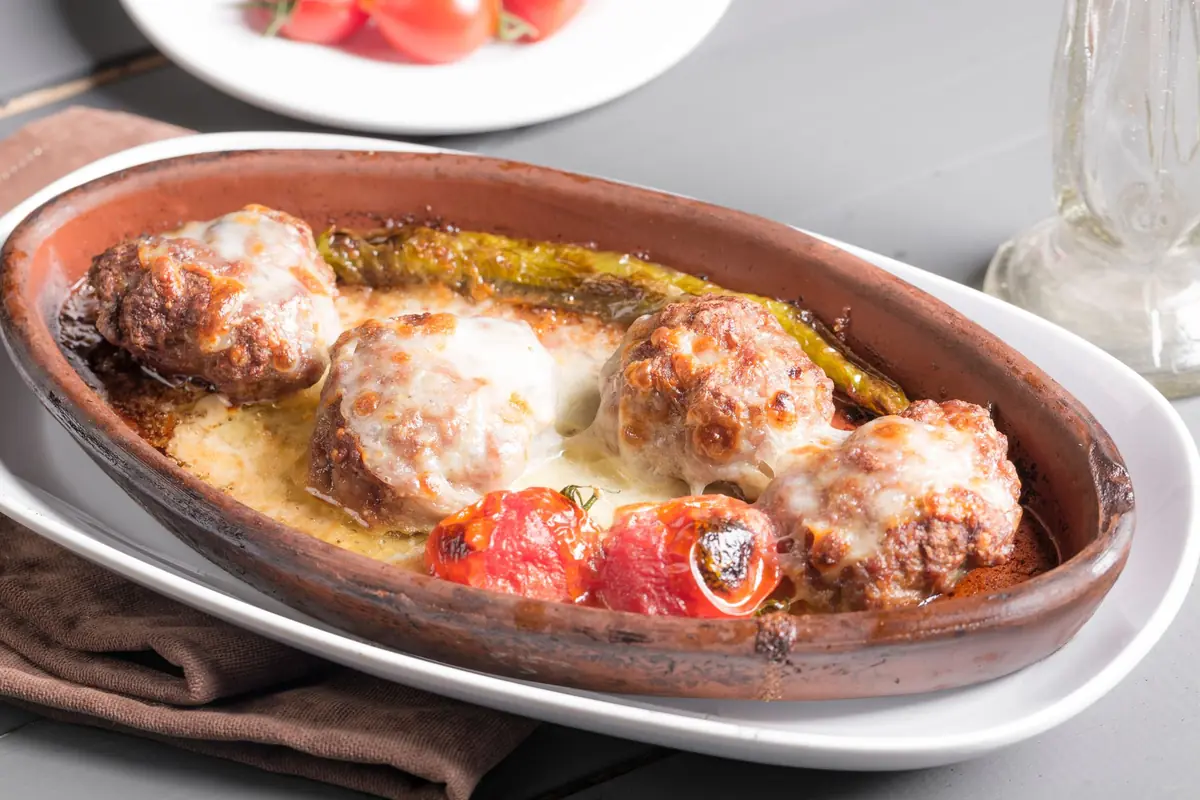 Delicious Turkish meatballs baked in a clay dish with tomatoes and peppers, perfect for authentic cuisine…