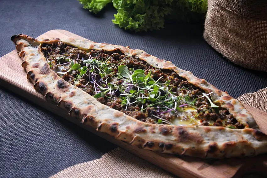 Delicious Turkish pide with savory minced meat and fresh greens on a wooden board.