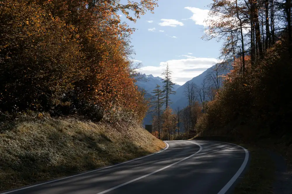 A picturesque view of an empty road winding through Swiss mountains in autumn.