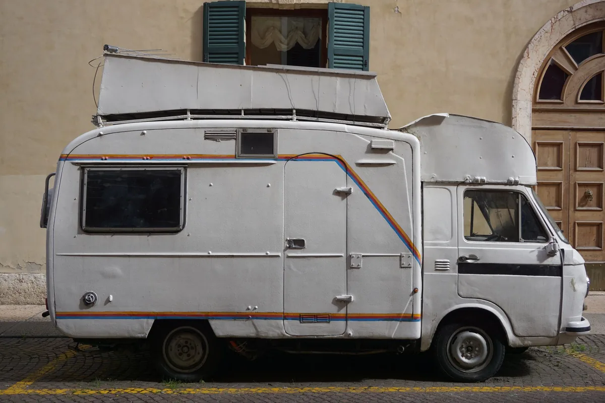 Side view of a vintage camper van against a stone building in Kotor, Montenegro.