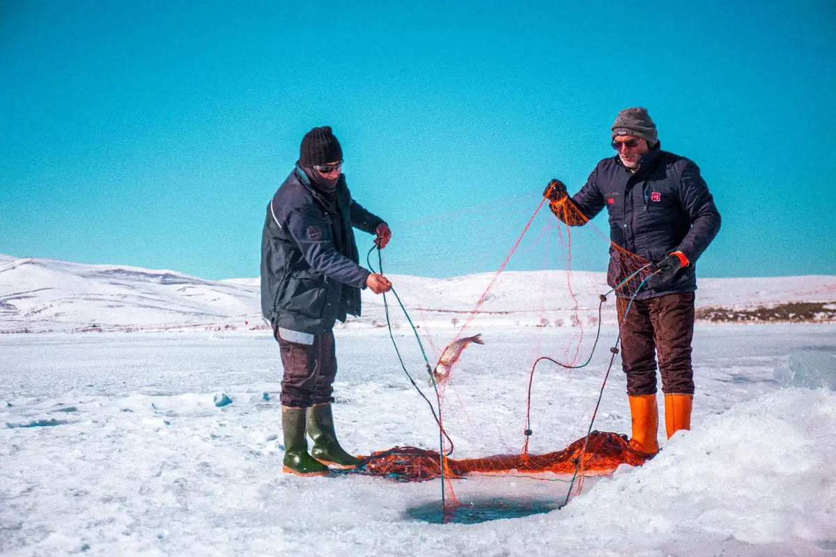 Two fishermen ice fishing on a frozen lake in Kars, Türkiye during winter.